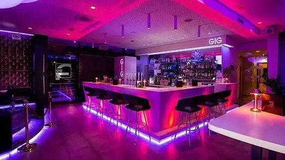 Back-bar bottle wall lit by an addressable RGB COB LED strip running a slow scene-drift sequence